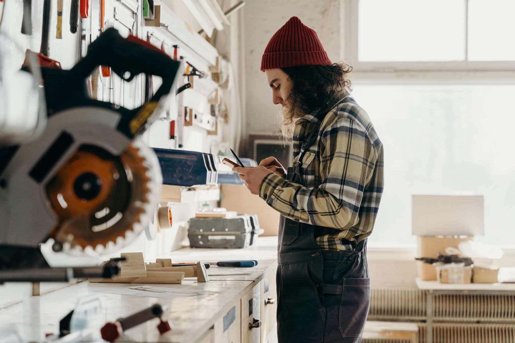 Independent carpenter checking a job on his phone in a working shop